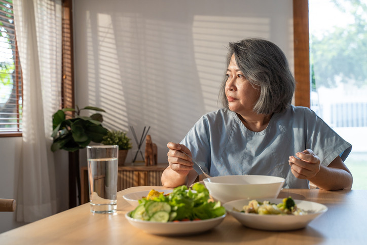 A mature Asian woman eating dinner alone at home. 