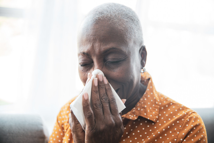 Senior Black woman holding a tissue, wiping her nose.