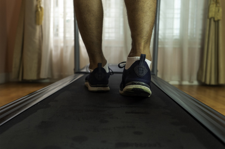 Close-up of a man wearing a blue sports walking on a treadmill in a private room.