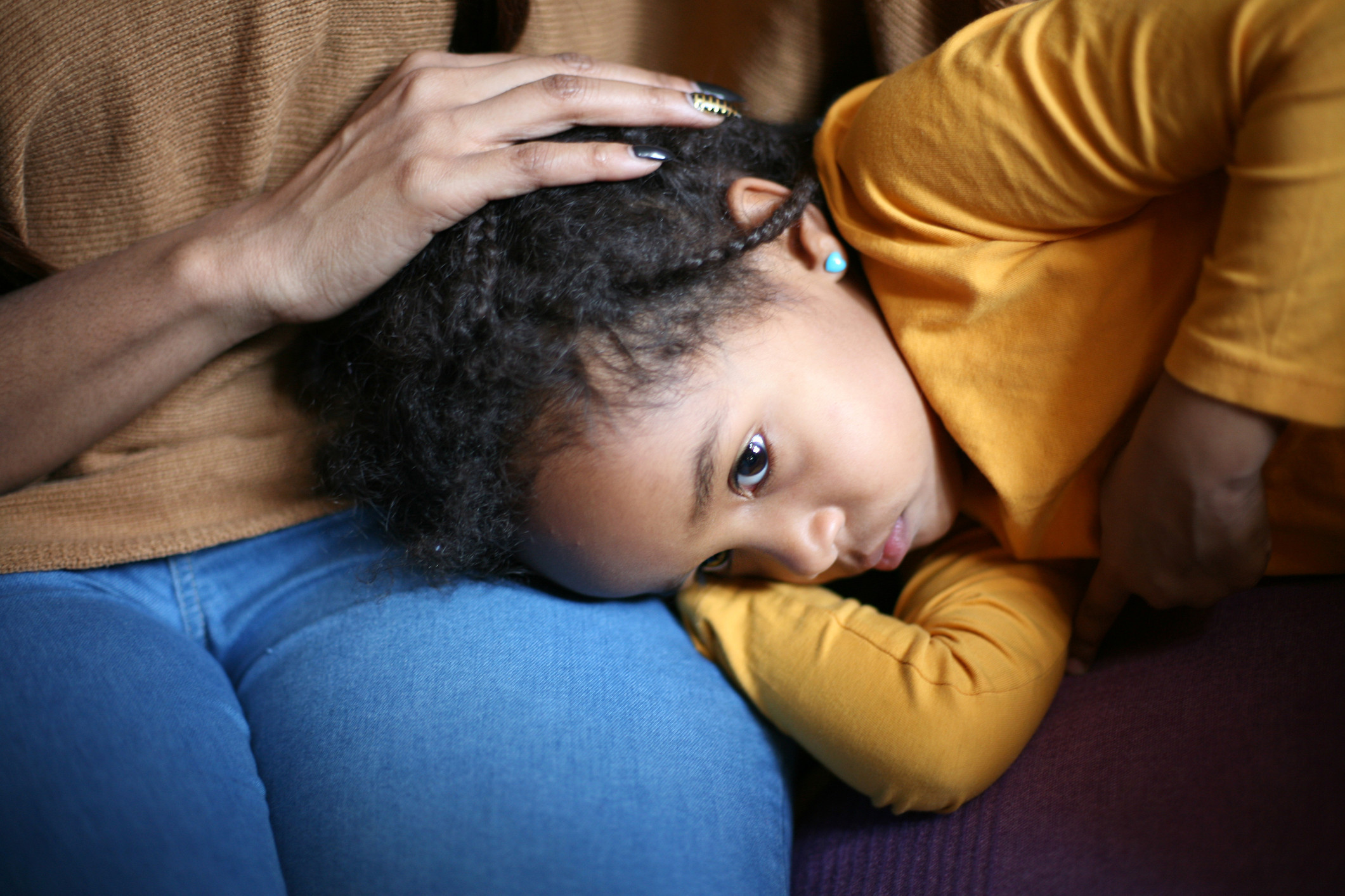 A young girl with a sad face laying on her mother's lap. 