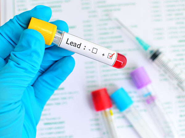 close up of gloved hand holding a vial containing a blood sample tested for lead exposure, with positive result marked on the side