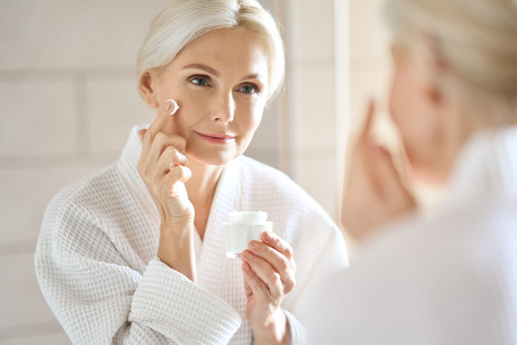 A mature woman looking in the mirror while applying cream to their face. 
