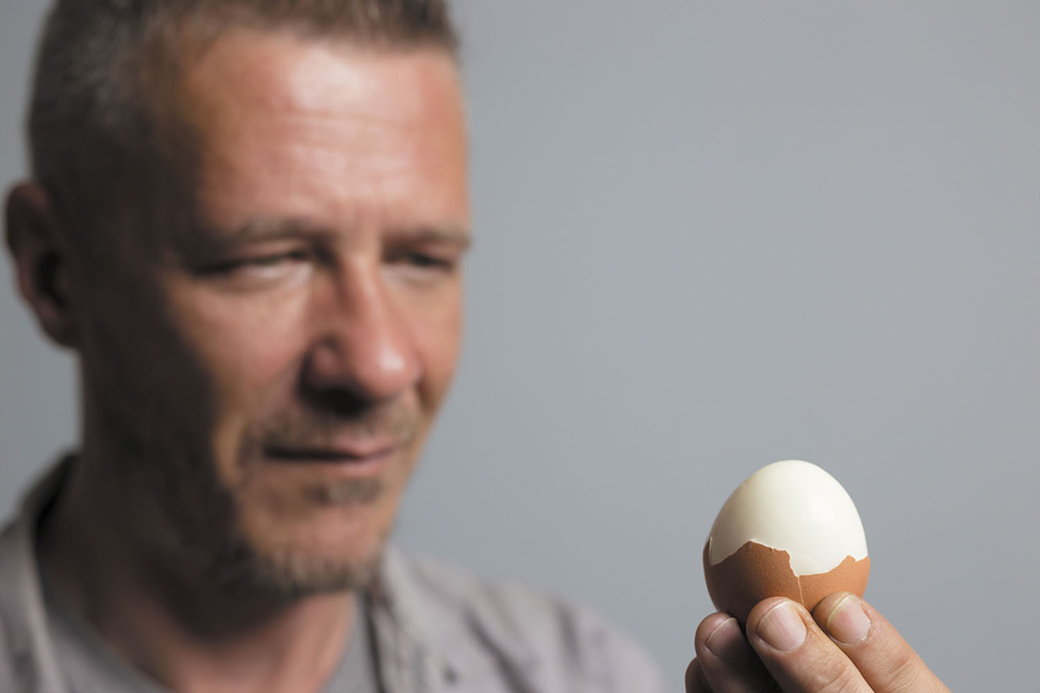 A man holding a half-cracked egg.