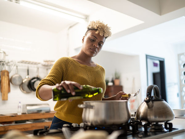 young woman cooking in her kitchen using olive oil