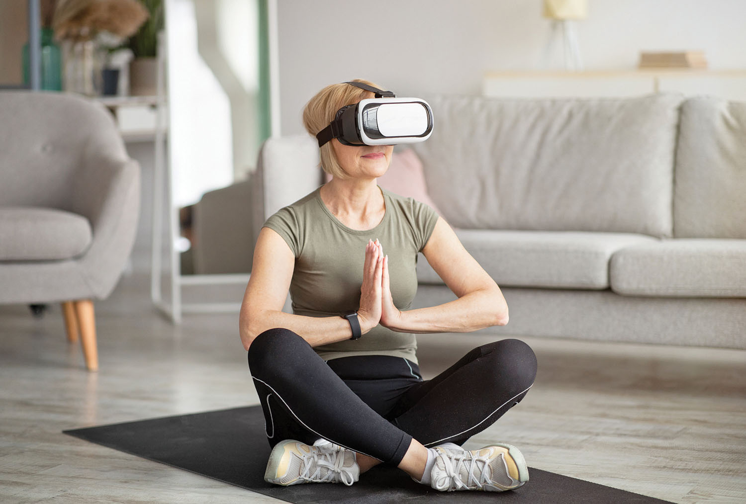 photo of a woman sitting cross-legged on the floor and holding her hands in a meditation-type position while wearing a virtual reality headset