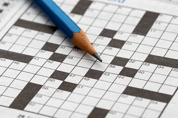 close-up photo of a crossword puzzle with none of the boxes filled in, and a sharpened blue pencil laid across it