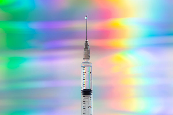 photo of a syringe filled with vaccine pointing upward, centered on a background of wavy psychedelic colors