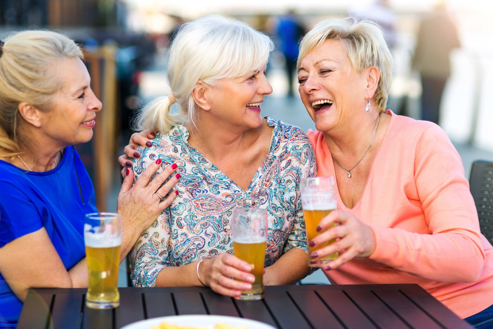 Three mature woman laughing while having beers together.