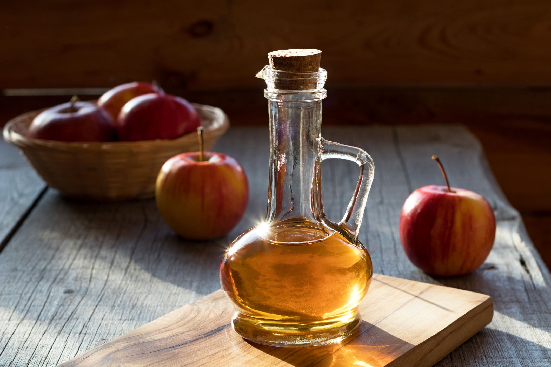 A bottle of apple cider vinegar in the morning sun, with apples in the background.