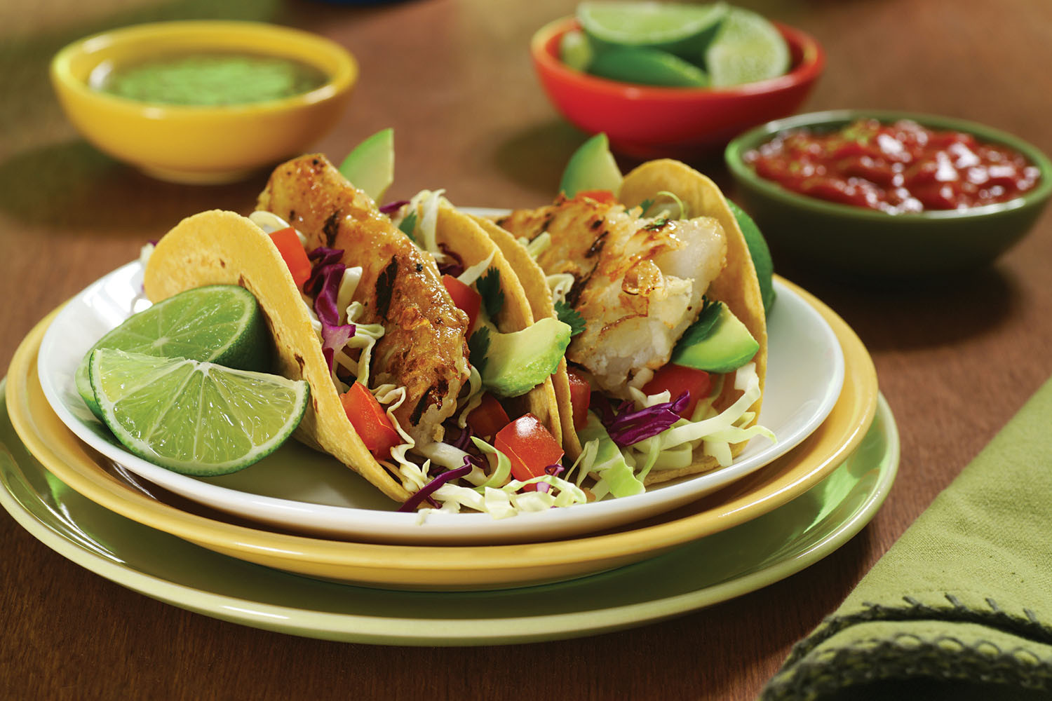 photo en gros plan d'une assiette de tacos avec des quartiers de citron vert sur le côté et des petits plats de sauces en arrière-plan