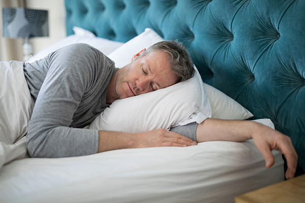 photo of a man sleeping on his left side, bed has a headboard upholstered in blue fabric