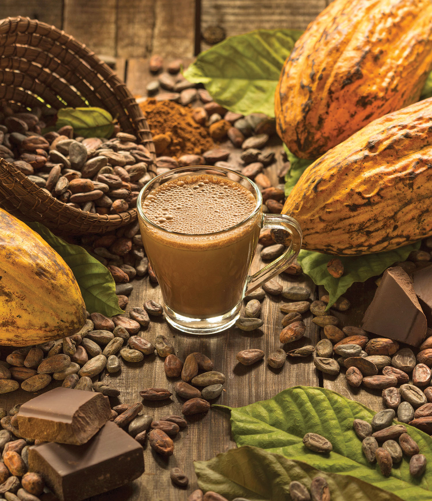 photo d'un assortiment de produits à base de fèves de cacao, avec une tasse en verre de cacao chaud au centre et des fèves en vrac éparpillées autour