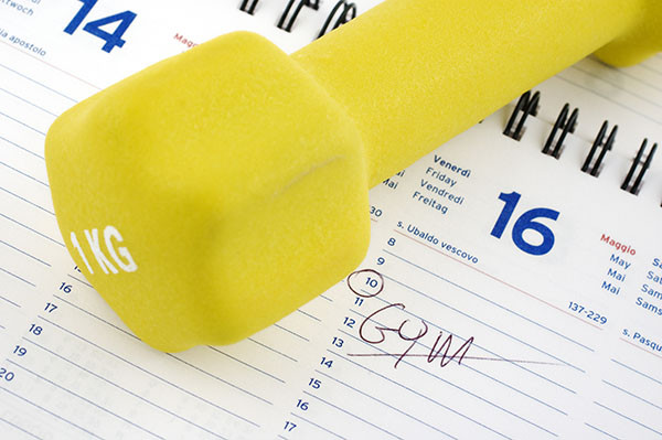 close-up photo of a yellow barbell marked 1 kilogram resting on top of a calendar with the word gym written in for the next day