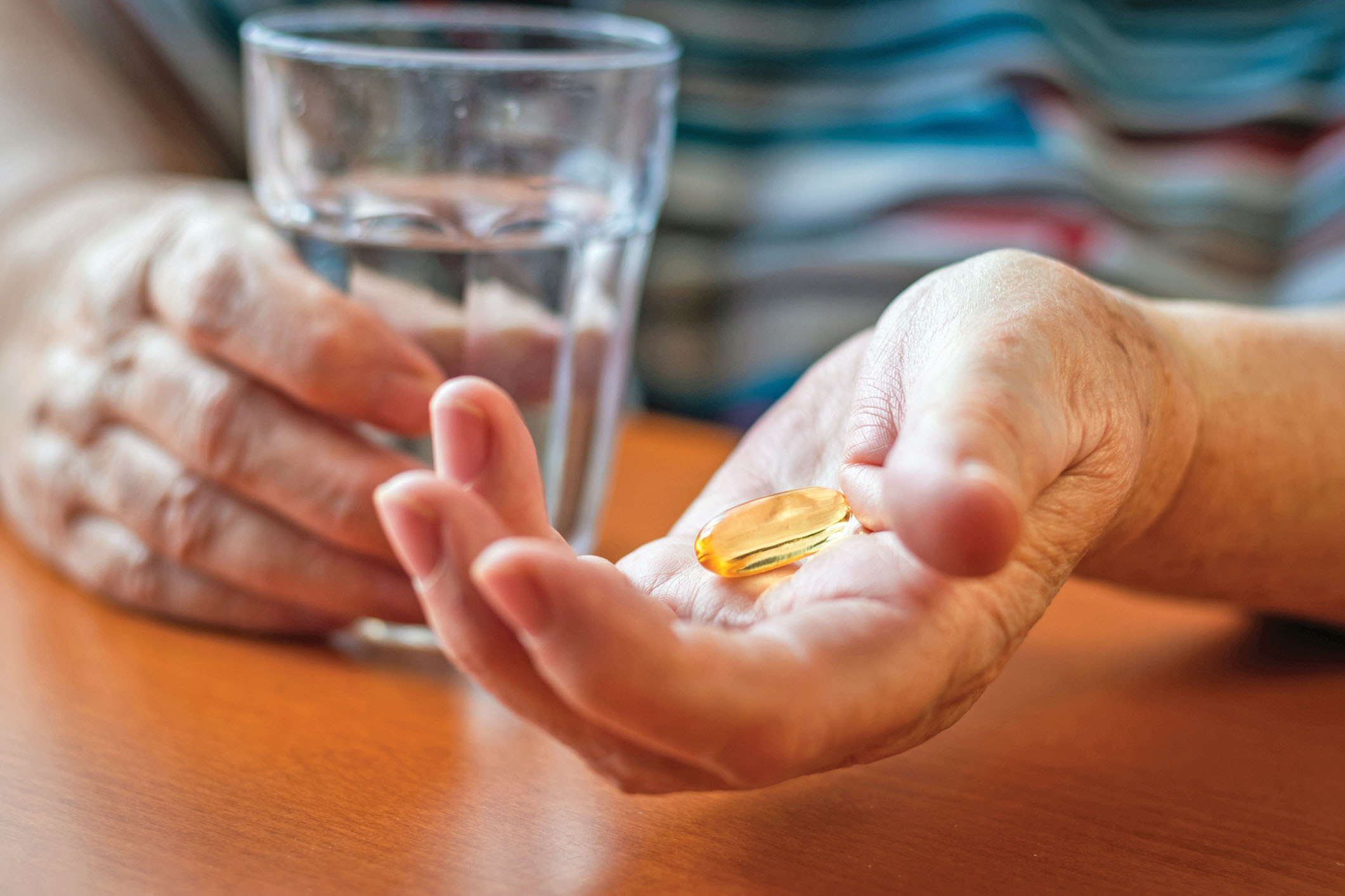 photo bien recadrée des mains d'une personne tenant un verre d'eau et une pilule jaune