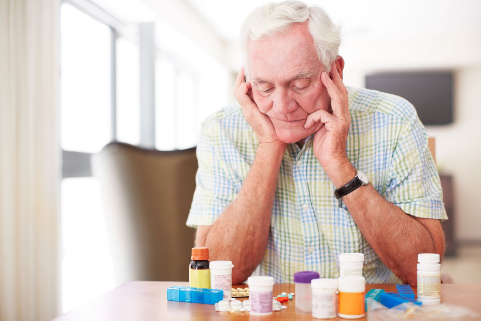 A picture of a senior male looking at various bottles of pills. 