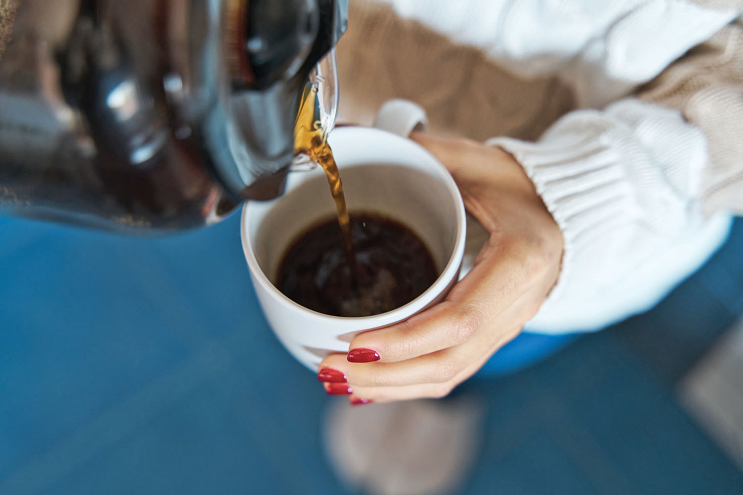 photo recadrée des mains d'une femme tenant une tasse dans sa main gauche et y versant du café à partir d'une carafe