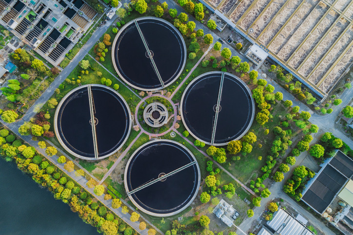 Aerial view of four tanks at a wastewater treatment plant with green trees and large-scale equipment dotted around the landscape