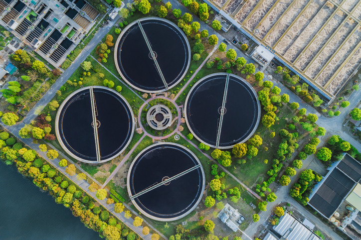 Vue aérienne de quatre réservoirs d'une usine de traitement des eaux usées avec des arbres verts et des équipements à grande échelle disséminés dans le paysage