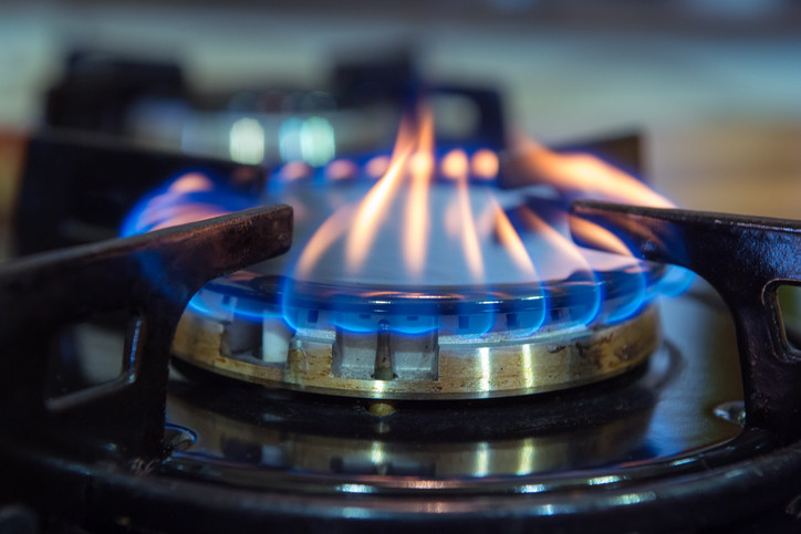 A gas stove burner with blue and yellowish flames; another burner in the background is blurred
