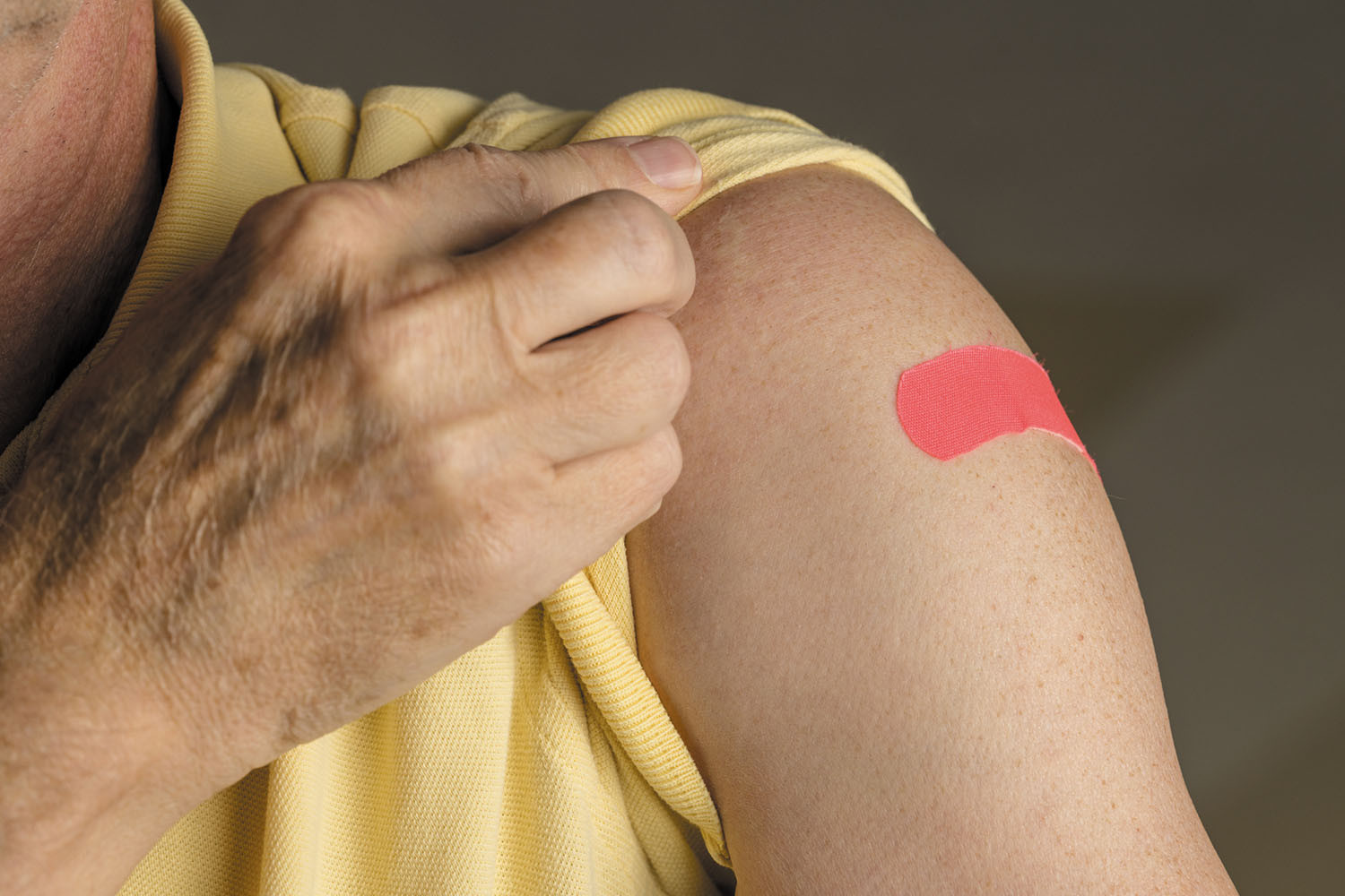 close-up photo of the upper arm of a person who has just received a vaccination and has a red bandage on the spot