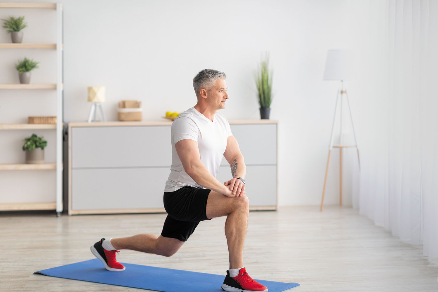 photo of a man doing a lunge exercise on a mat in his home