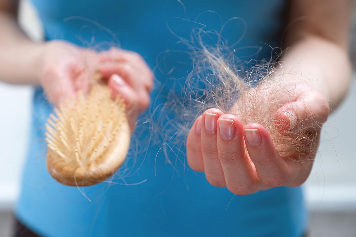 photo en gros plan des mains d'une femme tenant une brosse à cheveux dans la main droite et une touffe de cheveux dans la main gauche