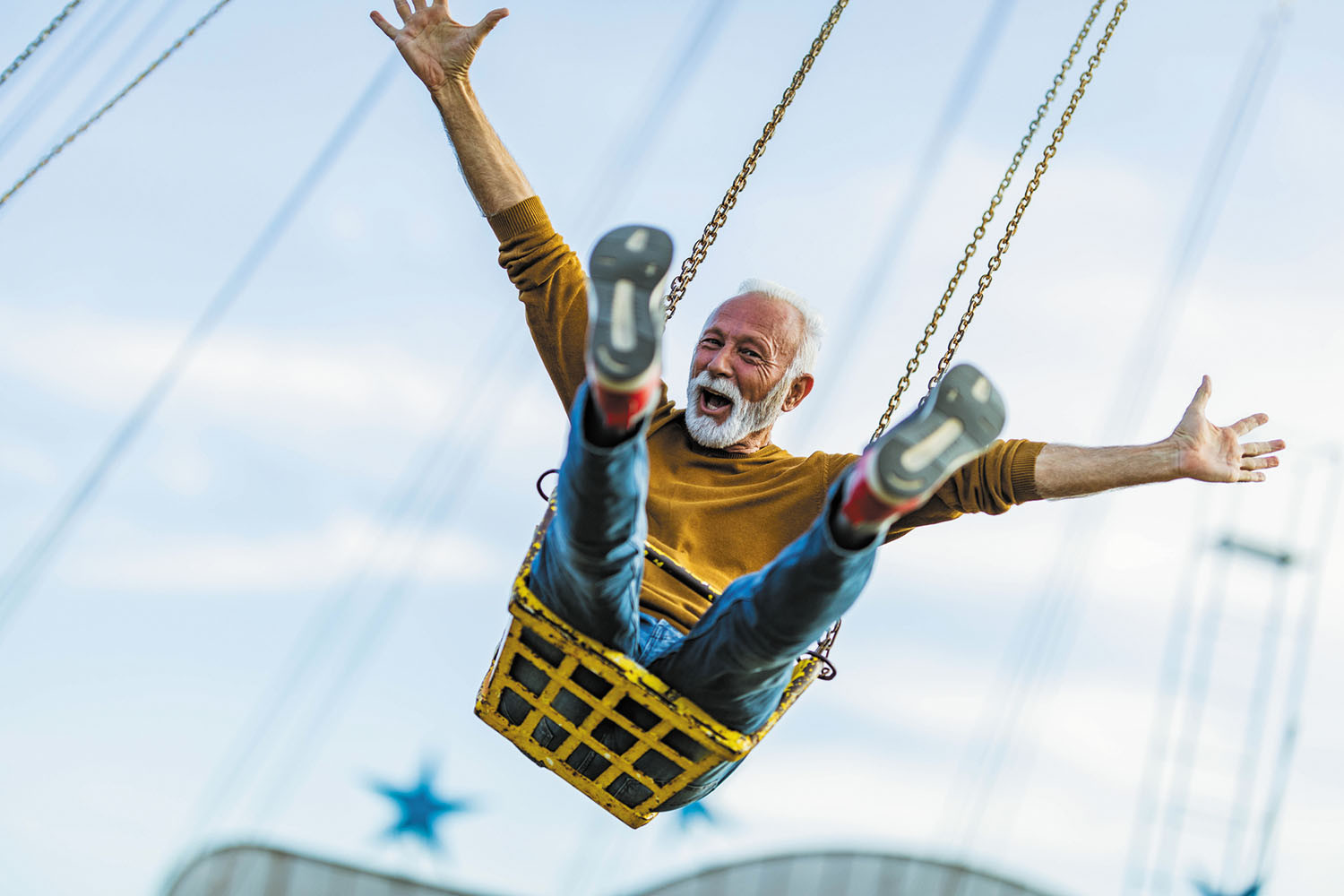 photo of a mature man outdoors on a swing, smiling and holding his arms out wide