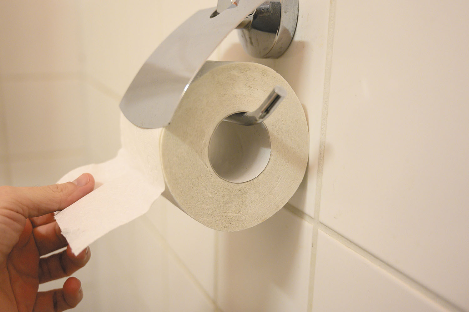 close-up photo of a roll of toilet paper with a hand reaching for it