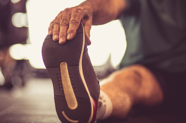 A mature man stretching his foot while sitting on the floor.