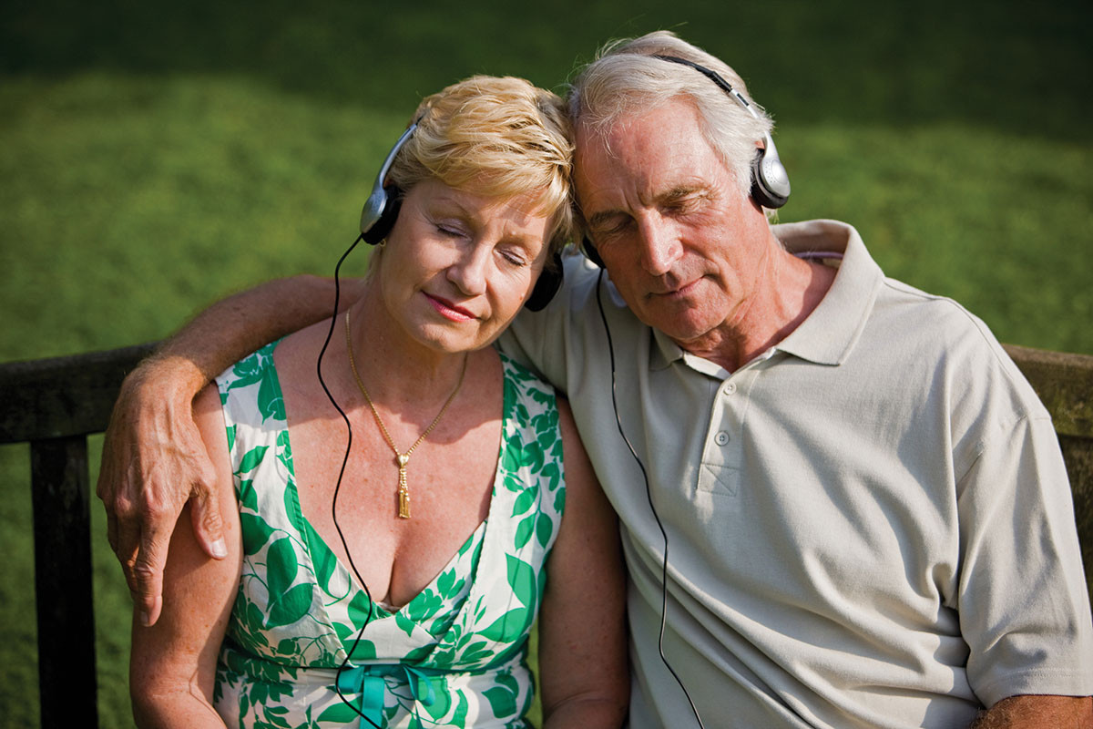 photo of a mature couple listening to music through headphones, sitting close to each other with their heads pressed together