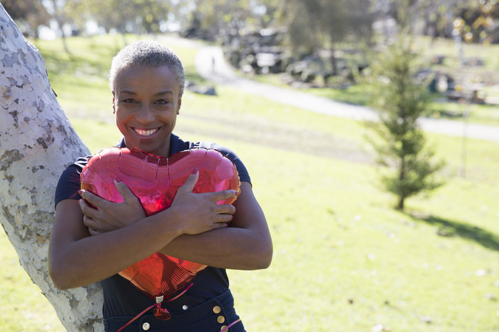 A photo of a mature woman hugging red heart-shaped balloon.