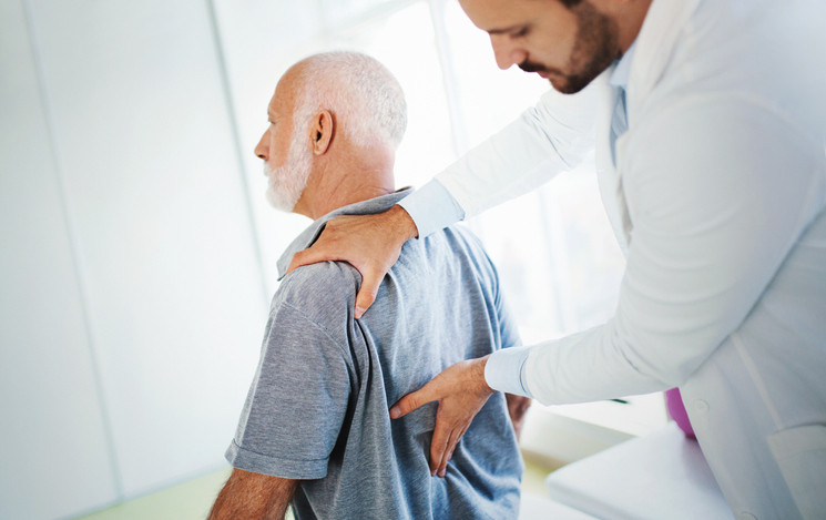A healthcare professional examining an elderly man's back. 