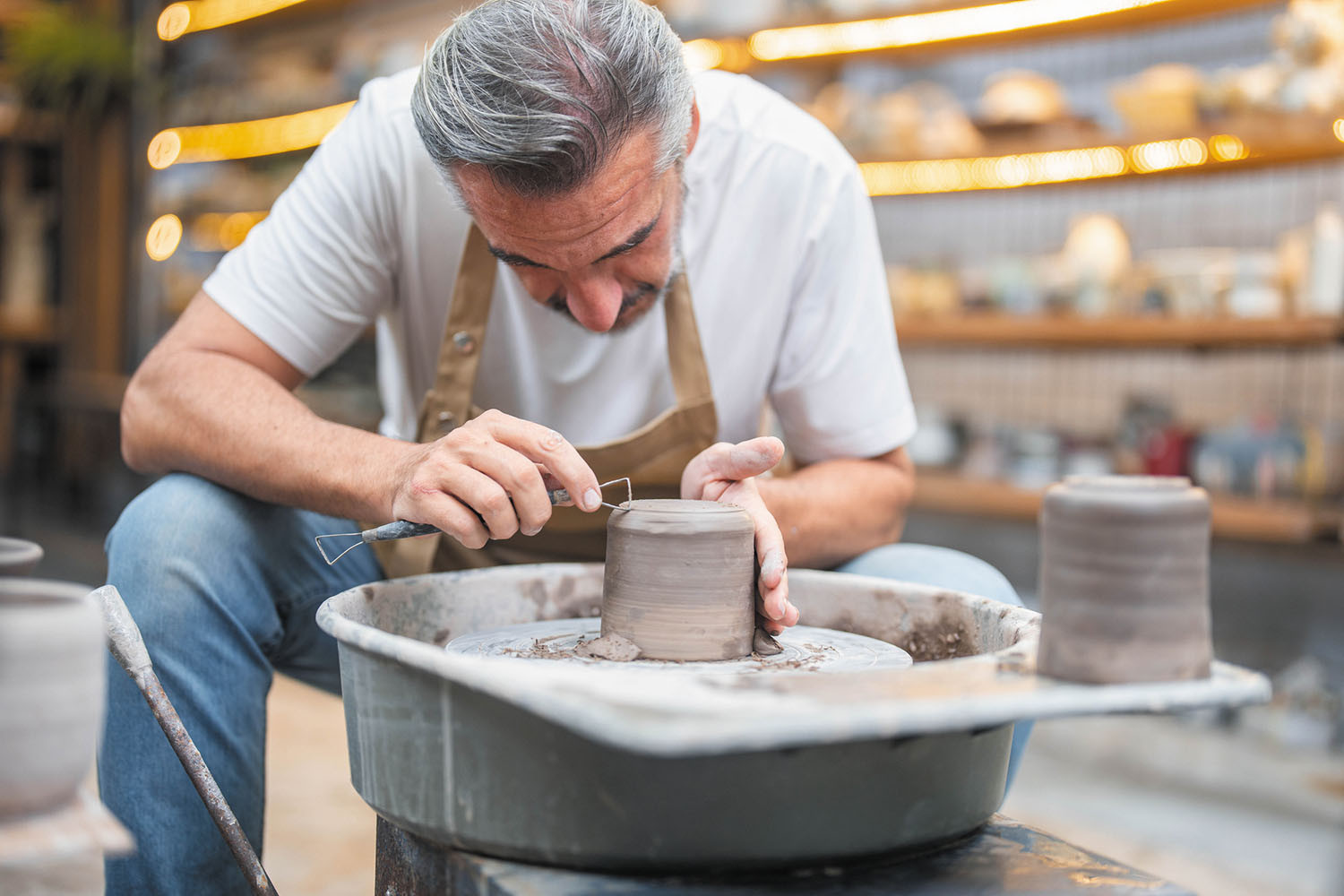 photo of a man bent over a pottery wheel as he uses a tool to shape the clay