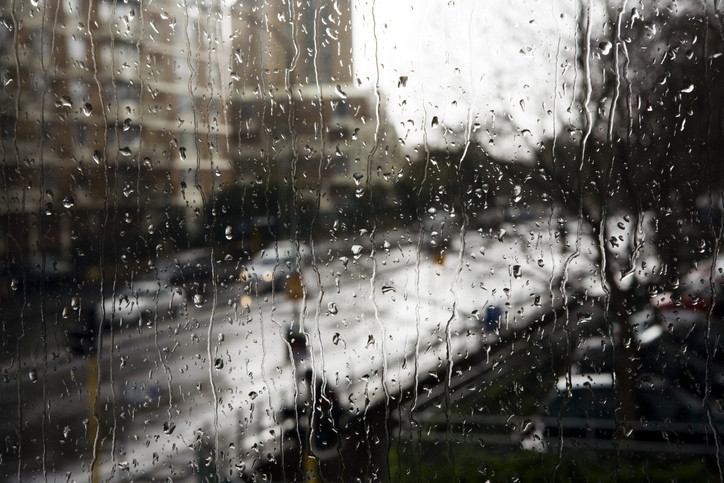 Raindrops rolling down a windowpane on a gray rainy day in a city