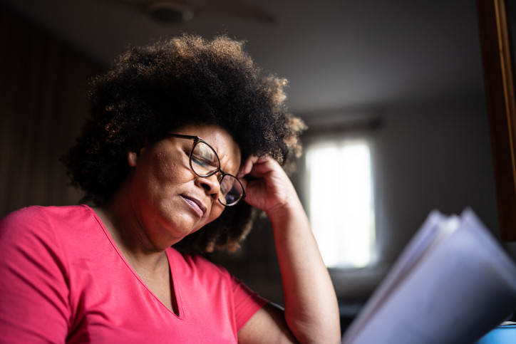 Une femme mature assise avec sa main posée sur son front et ses yeux fermés.