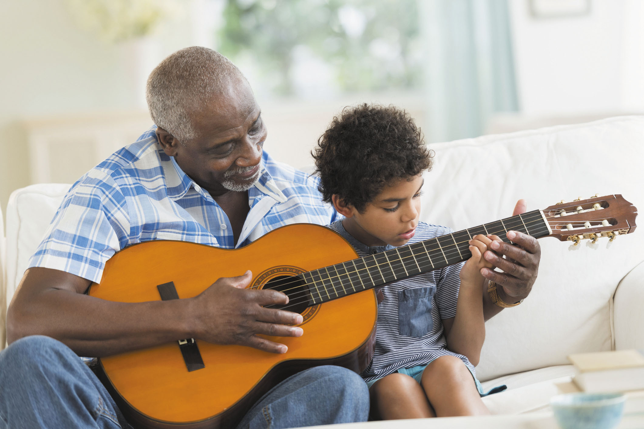 photo of a senior man showing his grandson how to play guitar