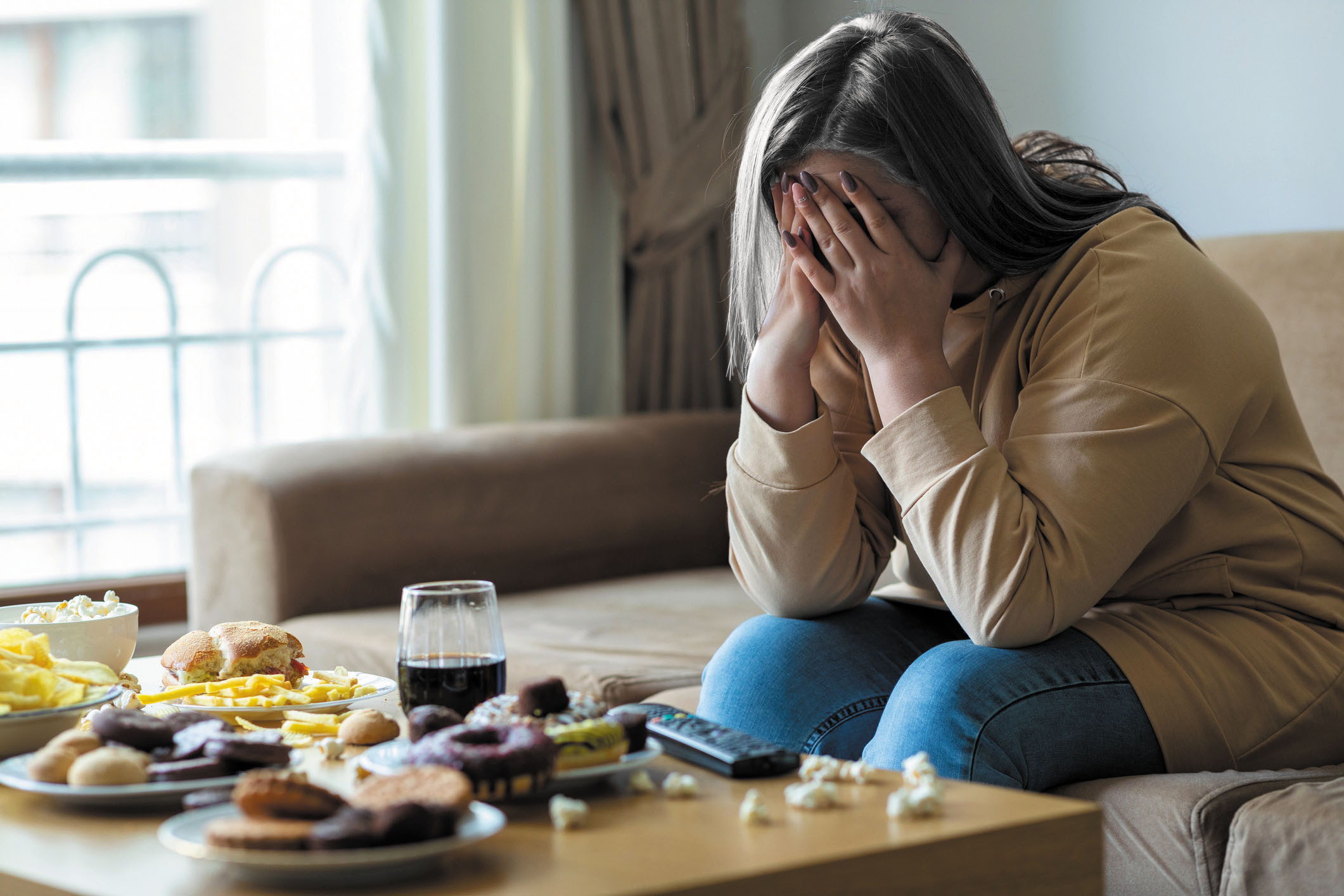 photo of a woman sitting on a couch holding her head in her hands with a spread of food on the coffee table in front of her