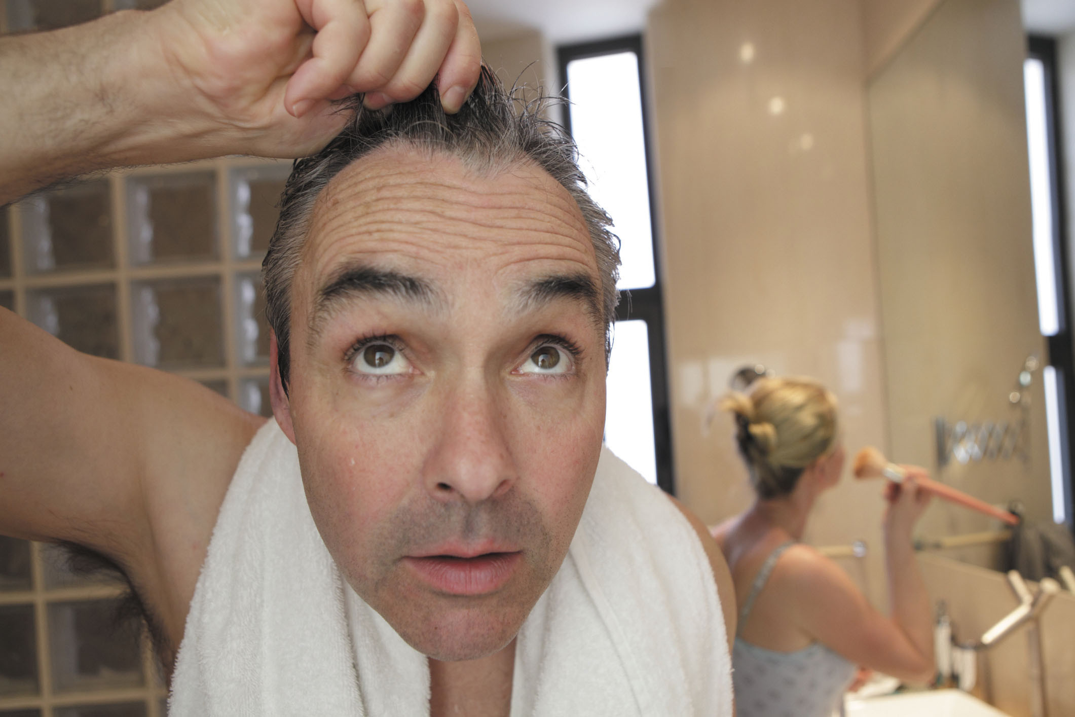 photo of a man looking in a mirror holding up some of his thinning hair
