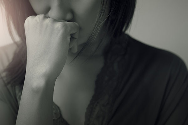 close-up photo of a woman looking troubled, holding her hand in a fist against her mouth