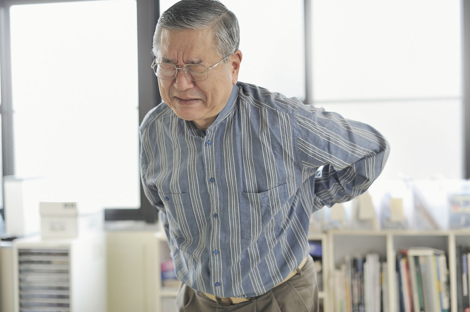 photo of a senior man wincing in pain and reaching his hand around to hold his back