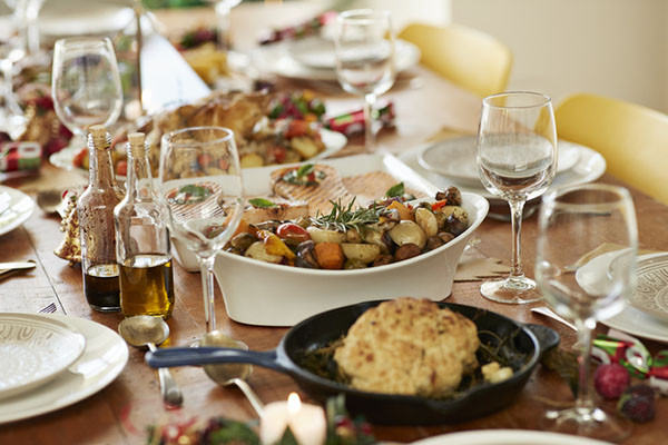 cropped photo showing a dish of roasted vegetables among other dishes on a table set for a holiday dinner, with glasses of water and wine also visible