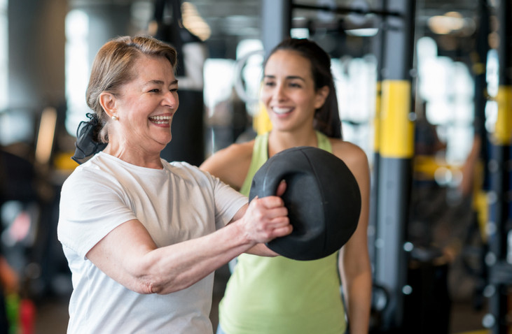 Adult woman exercising at the gym with a personal trainer and looking very happy