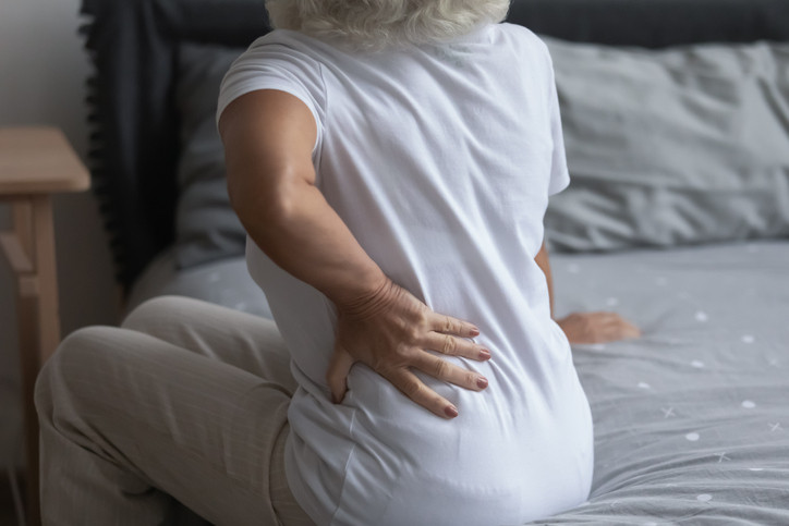 Close up unhealthy mature woman touching back, sitting on bed