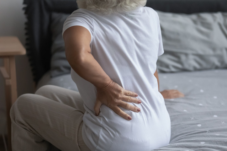 Gros plan sur une femme mûre malsaine touchant le dos, assise sur le lit