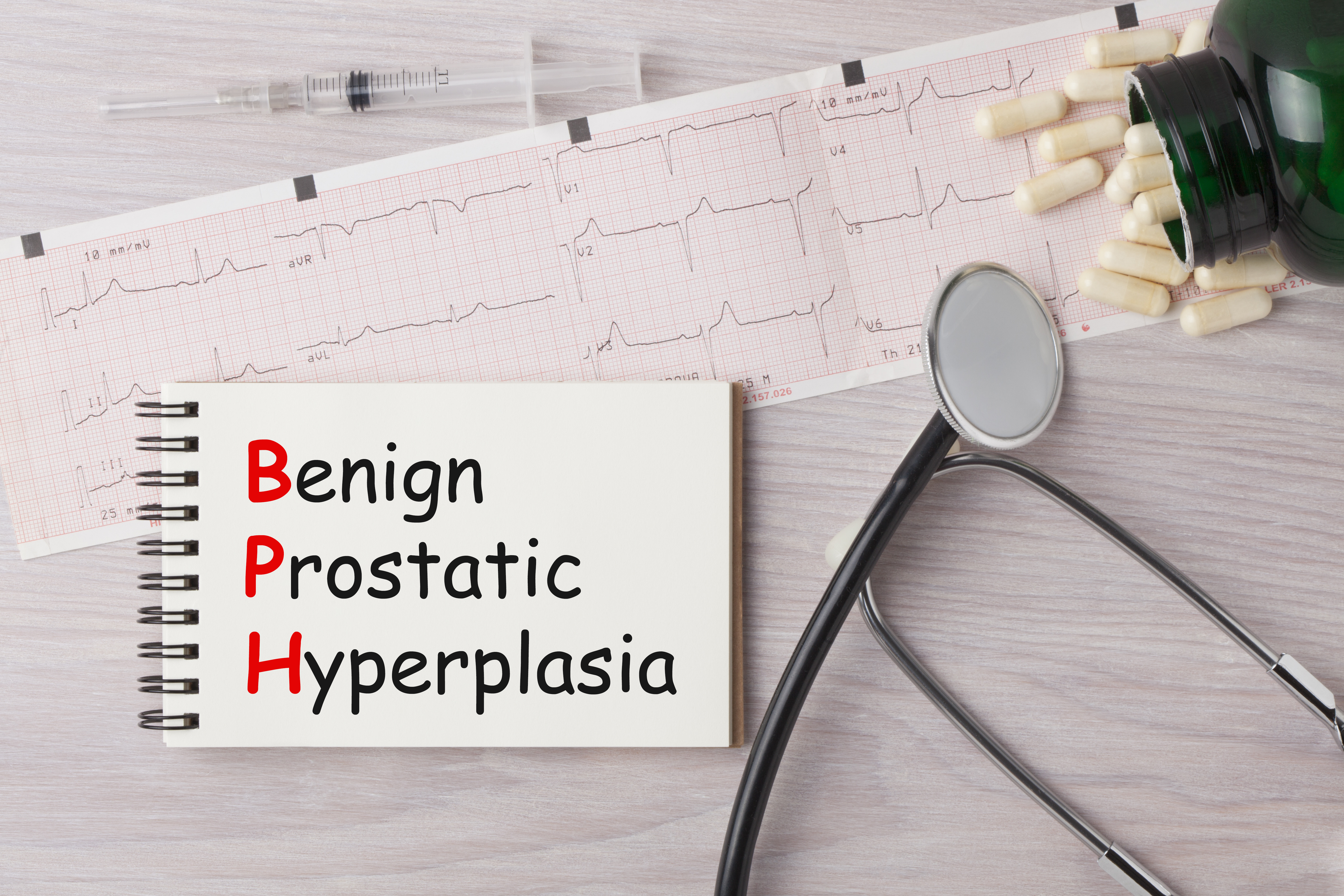 BPH- Benign Prostatic Hyperplasia written on notebook with stethoscope, syringe, eyeglasses and pills.