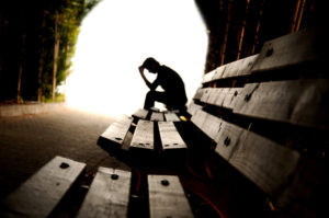 The silhouette of a man in a tunnel, he's sitting on bench, leaning forward with his hand to his head