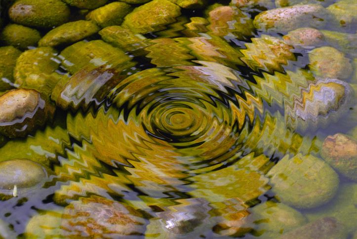 A body of water, at the bottom there are rocks, on the water's surface the water is rippled in a circular pattern