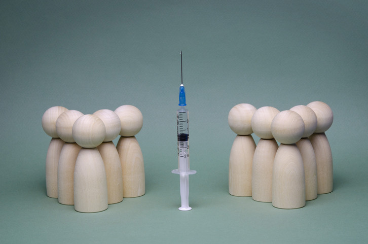 Photo of two separate groups of wooden figures with vaccine syringe between them