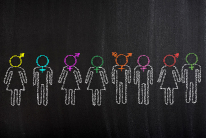 illustration resembling a chalk drawing of a line of figures on a black background with a variety of gender identity symbols in different colors for heads