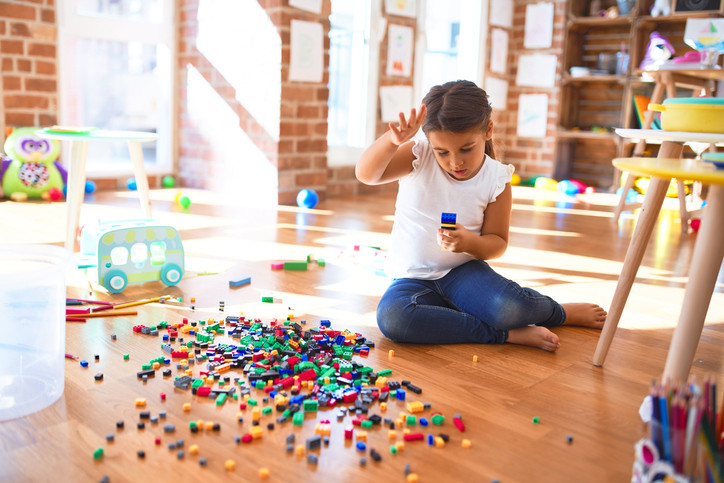 A child in a playroom with toys are scattered all over the floor